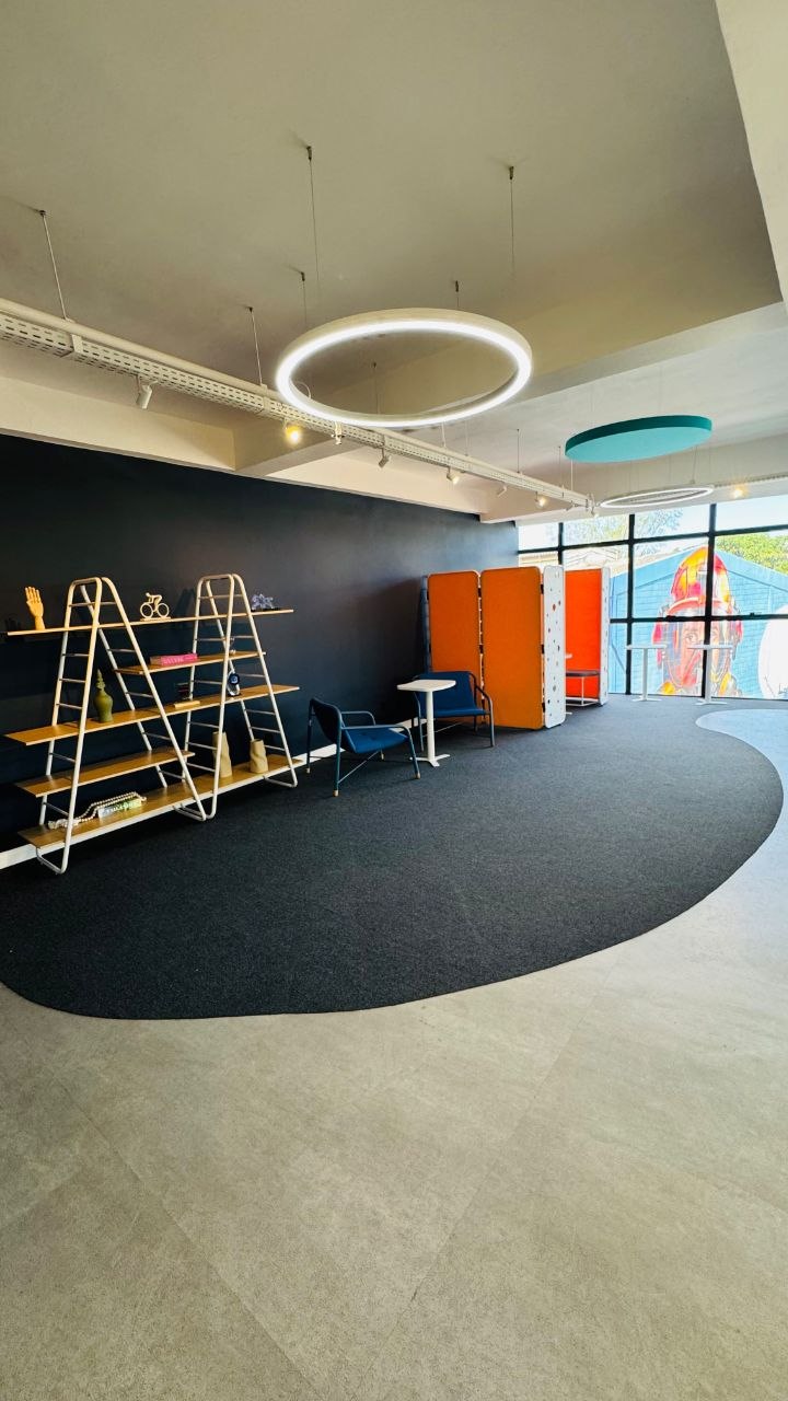 Lounge corporativo com parede preta, estante metálica, poltronas azuis e luminárias circulares